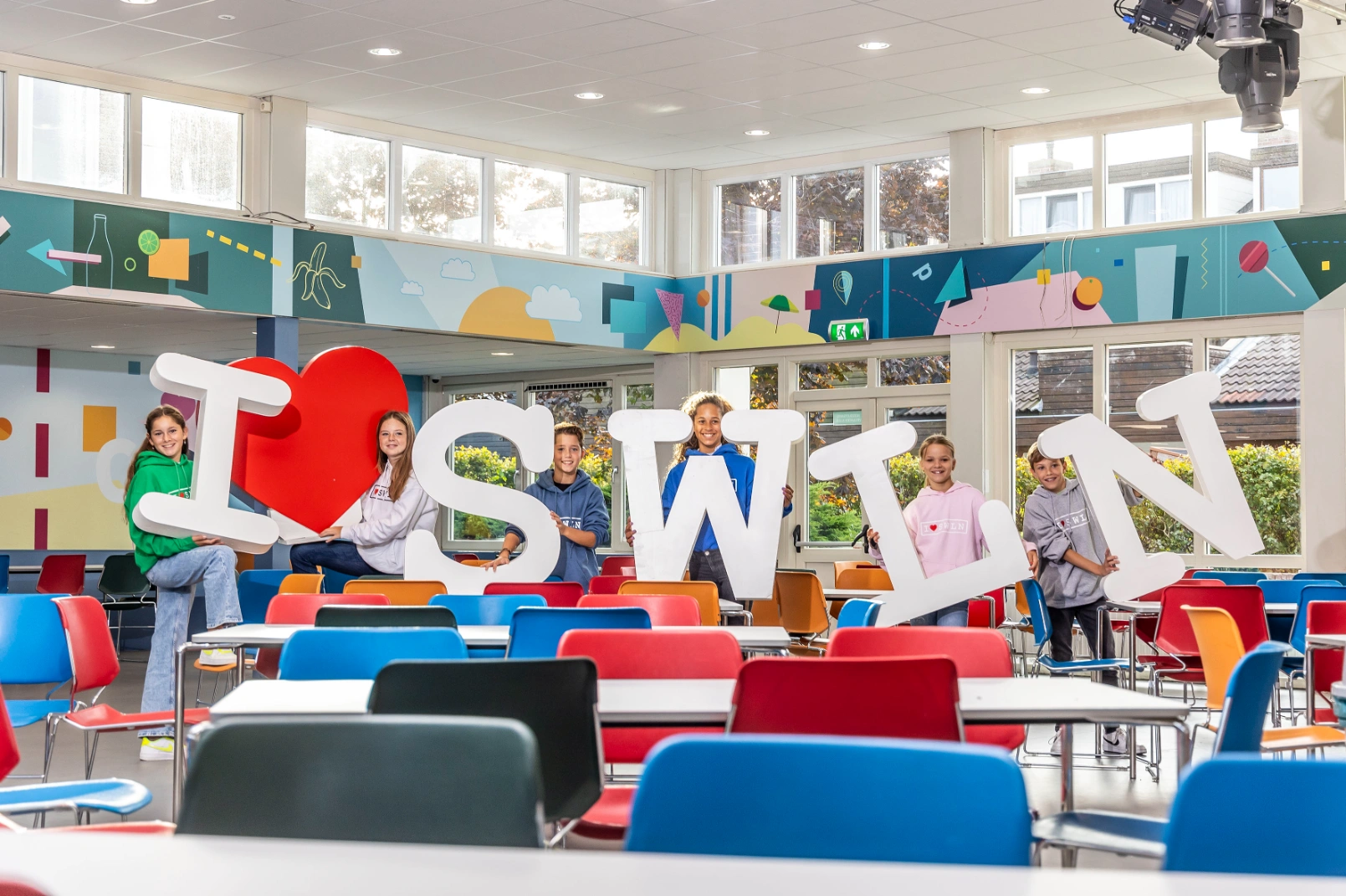 Leerlingen van ISW Sweelincklaan poseren met grote letters die samen de tekst ‘I ❤️ SWLN’ vormen in de aula.
